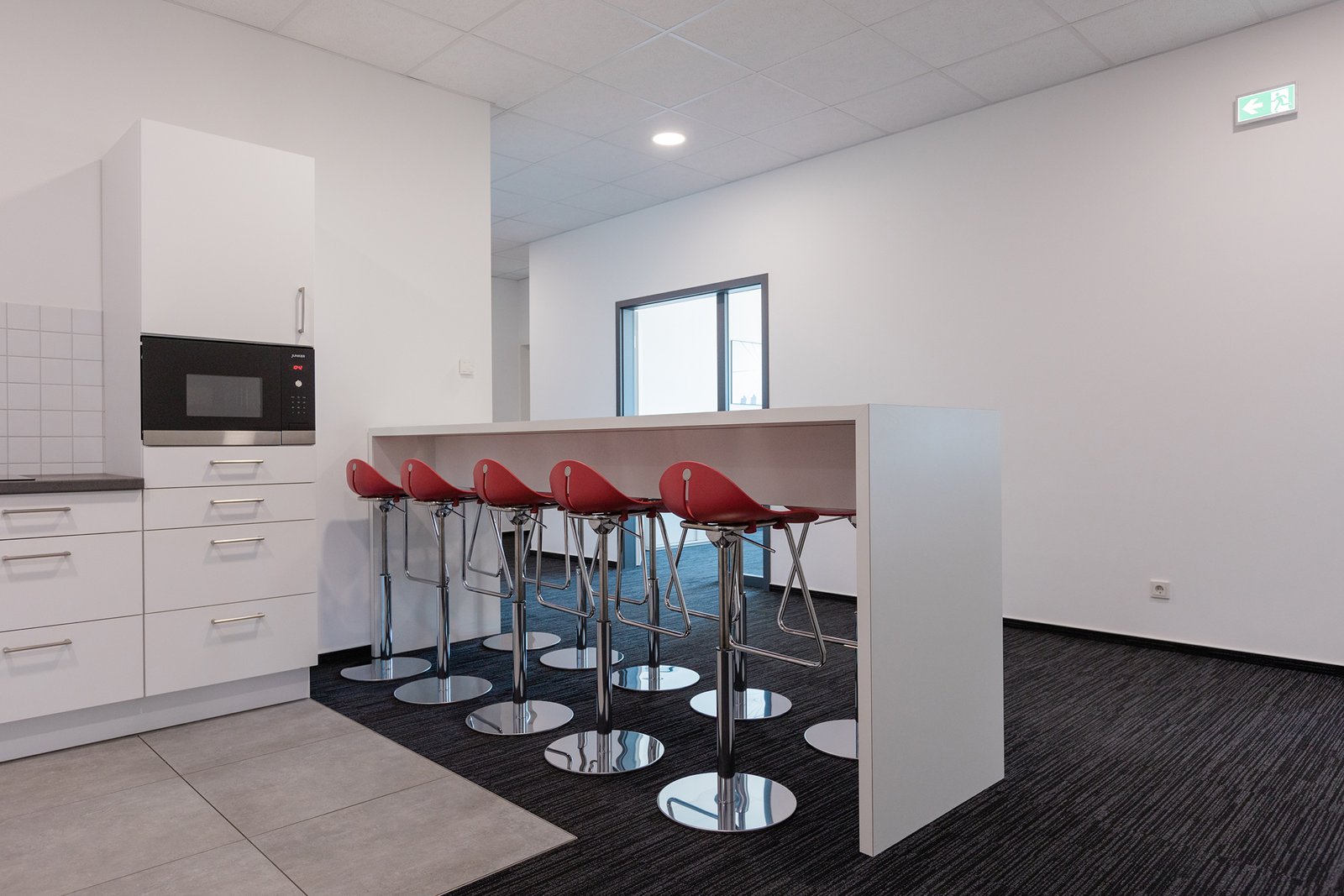 Moderne Küche mit Stehtisch, fünf roten Hockern und KTW-Kanzleiflair in einem hellen Raum.