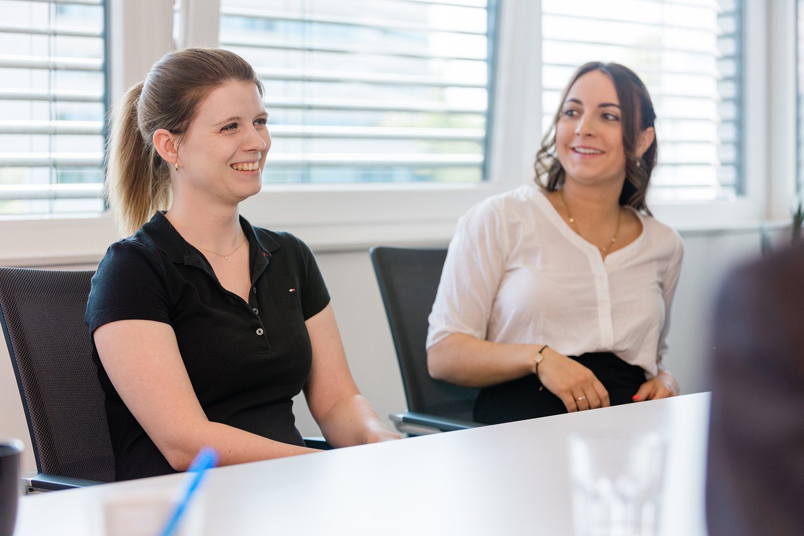 Zwei Frauen, wahrscheinlich Steueberaterinnen, plaudern und lächeln in einer hellen Büroumgebung miteinander. Zwei Frauen, wahrscheinlich Steueberaterinnen, plaudern und lächeln in einer hellen Büroumgebung miteinander.