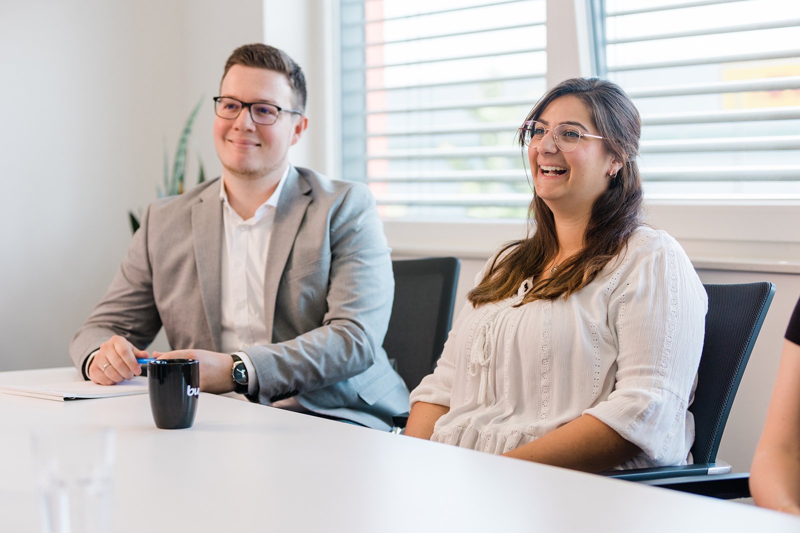 Zwei Personen sitzen lächelnd an einem Besprechungstisch, während KTW Wirtschaftsprüfer am Fenster zuhören. Zwei Personen sitzen lächelnd an einem Besprechungstisch, während KTW Wirtschaftsprüfer am Fenster zuhören.